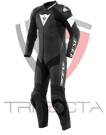 Black Dainese motorcycle racing suit with white accents, featuring the Dainese logo on the chest, arms, and legs. The suit is a one-piece design with integrated protective elements at the shoulders, elbows, and knees. The background includes a faint grey Dainese demon logo and the word ‘TRIFECTA’ in bold grey letters at the bottom.